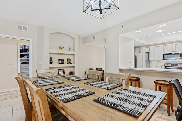 dining room featuring light wood-type flooring, built in features, an inviting chandelier, and sink