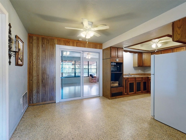 kitchen featuring white refrigerator, sink, ceiling fan, and wooden walls