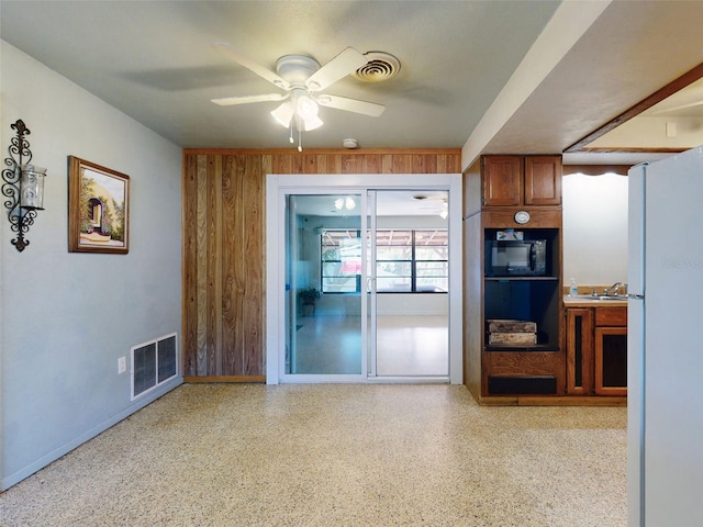 kitchen with white refrigerator, black microwave, ceiling fan, and wooden walls