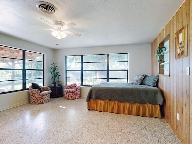 bedroom featuring a textured ceiling, ceiling fan, and wood walls