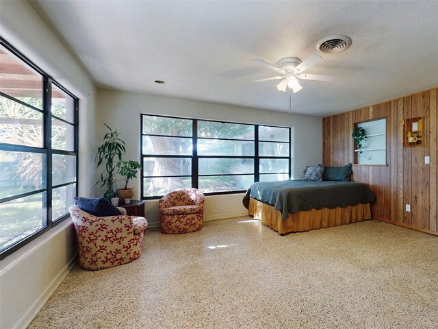 bedroom with a textured ceiling, ceiling fan, wooden walls, and multiple windows