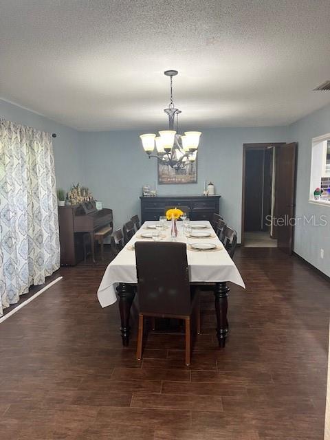 dining area with dark wood-type flooring, a notable chandelier, and a textured ceiling