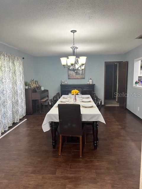 dining space with a textured ceiling, a notable chandelier, and dark hardwood / wood-style flooring