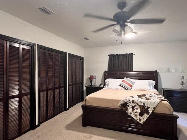 carpeted bedroom with ceiling fan and multiple closets