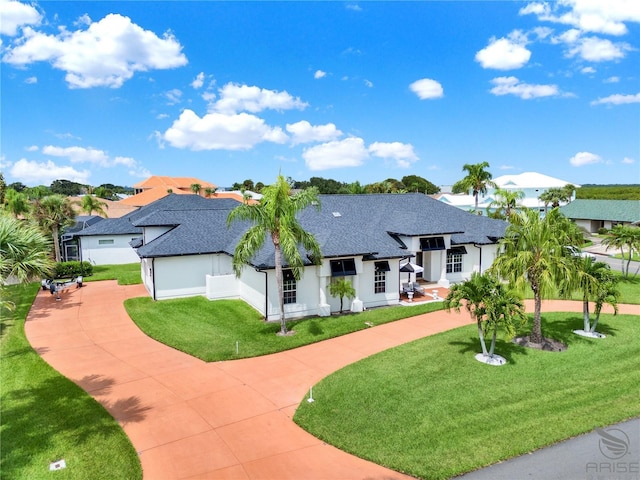 view of front of property with a shingled roof, a front yard, and curved driveway