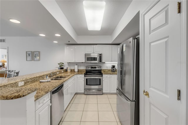 kitchen with appliances with stainless steel finishes, kitchen peninsula, sink, light stone counters, and white cabinets