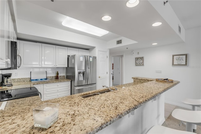 kitchen with light tile patterned floors, light stone countertops, stainless steel appliances, white cabinetry, and sink