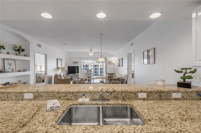 kitchen featuring built in features, ceiling fan, sink, and light stone countertops