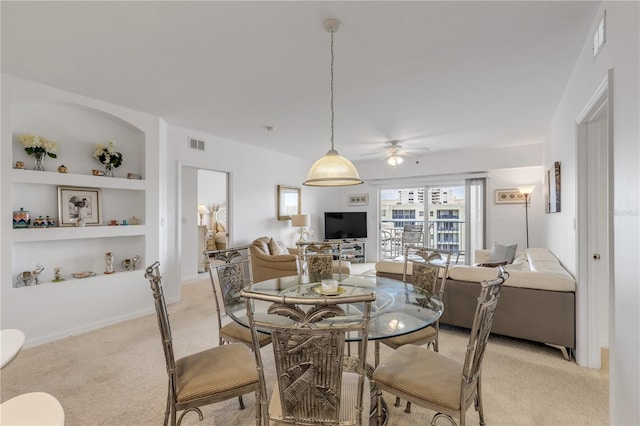 dining room featuring built in shelves, ceiling fan, and light carpet