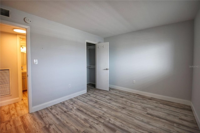 unfurnished bedroom with light wood-type flooring, a walk in closet, and a closet