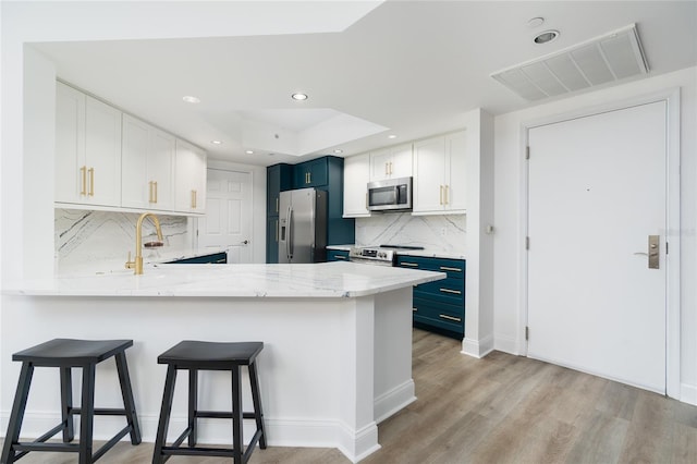 kitchen featuring light hardwood / wood-style floors, tasteful backsplash, stainless steel appliances, kitchen peninsula, and white cabinetry