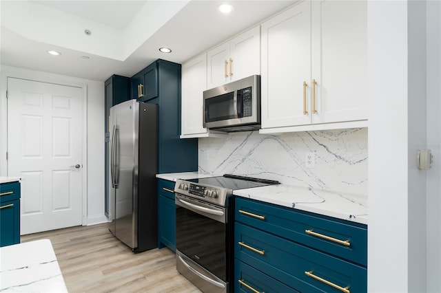 kitchen with white cabinets, blue cabinetry, appliances with stainless steel finishes, light hardwood / wood-style floors, and tasteful backsplash