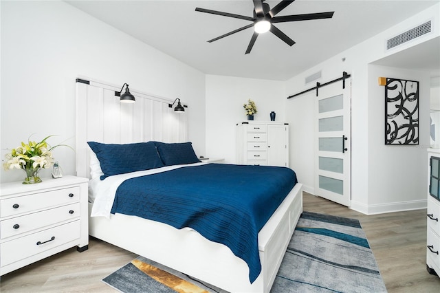 bedroom featuring light hardwood / wood-style floors, ceiling fan, and a barn door