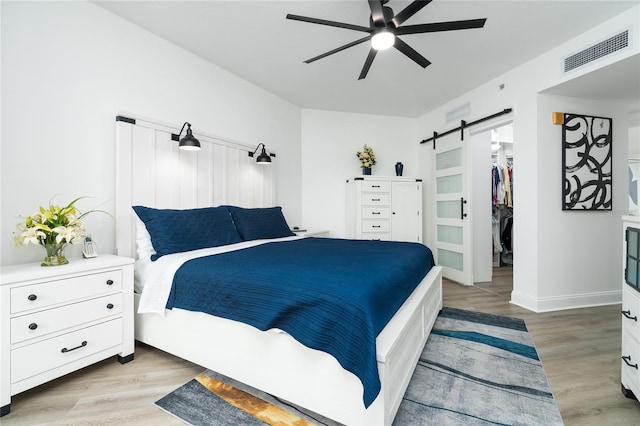 bedroom with a barn door, ceiling fan, a spacious closet, and light hardwood / wood-style flooring