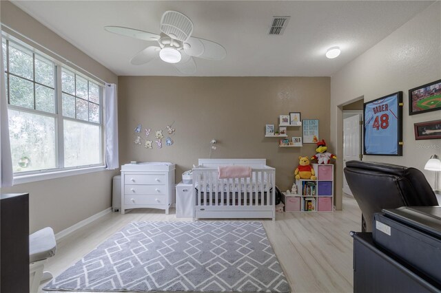 bedroom featuring light hardwood / wood-style flooring, a nursery area, and ceiling fan