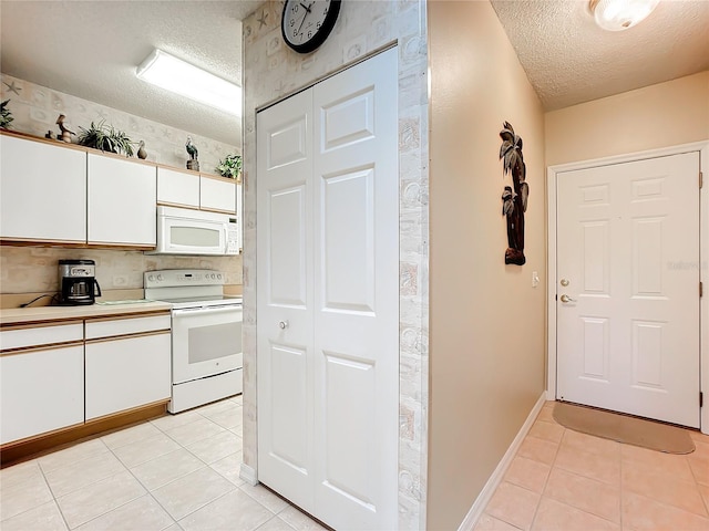 kitchen featuring white appliances, light tile patterned floors, white cabinets, and a textured ceiling