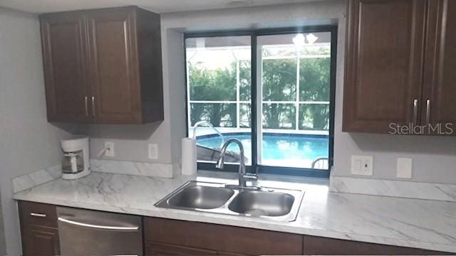 kitchen with light stone counters, stainless steel dishwasher, dark brown cabinetry, and sink