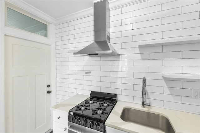 kitchen featuring gas stove, sink, white cabinets, wall chimney range hood, and crown molding