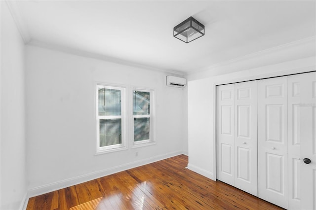 unfurnished bedroom featuring an AC wall unit, a closet, hardwood / wood-style flooring, and ornamental molding