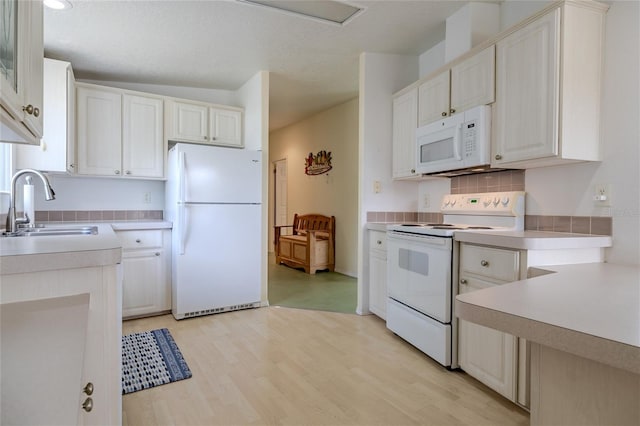 kitchen with white cabinets, sink, white appliances, light hardwood / wood-style floors, and decorative backsplash