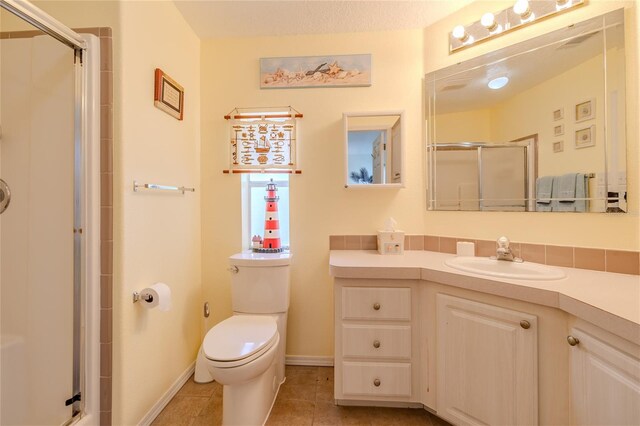 bathroom featuring vanity, toilet, a shower with door, and tile patterned floors