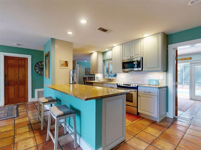 kitchen featuring decorative backsplash, sink, a breakfast bar, appliances with stainless steel finishes, and light stone counters