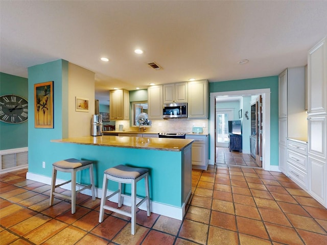 kitchen featuring kitchen peninsula, backsplash, appliances with stainless steel finishes, a kitchen breakfast bar, and sink