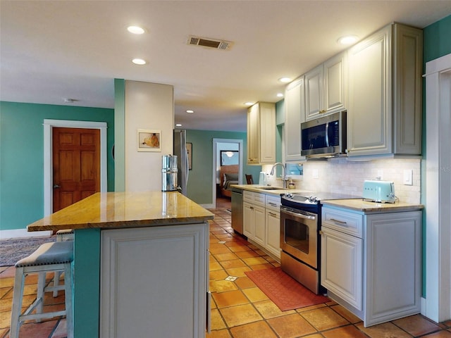 kitchen featuring a kitchen island, stainless steel appliances, sink, white cabinetry, and tasteful backsplash