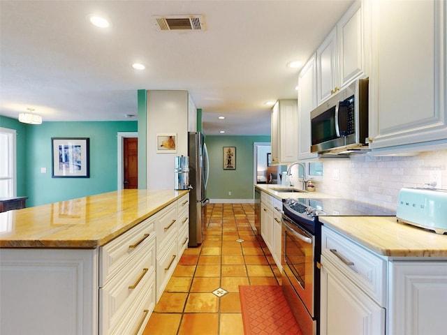 kitchen featuring sink, stainless steel appliances, white cabinets, decorative backsplash, and light tile patterned floors