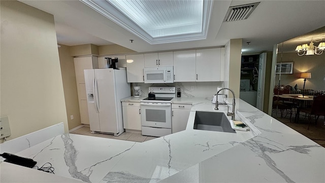 kitchen with sink, white appliances, white cabinetry, light stone countertops, and decorative backsplash