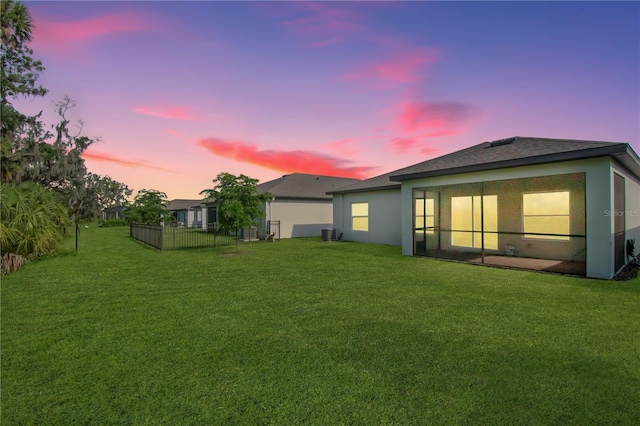 back house at dusk featuring a lawn and central AC