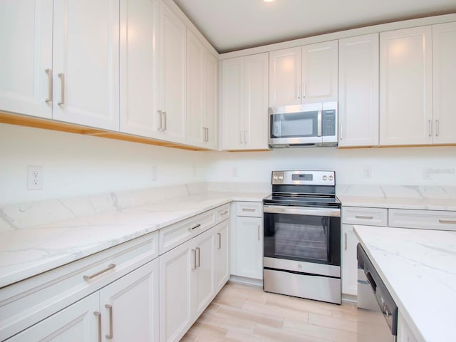 kitchen with light hardwood / wood-style flooring, stainless steel appliances, light stone countertops, and white cabinetry