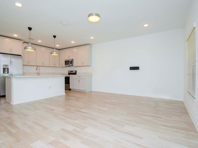 kitchen with pendant lighting, light wood-type flooring, a kitchen island with sink, white cabinetry, and appliances with stainless steel finishes