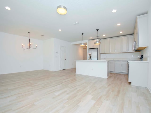 kitchen with appliances with stainless steel finishes, hanging light fixtures, light hardwood / wood-style floors, white cabinets, and a kitchen island