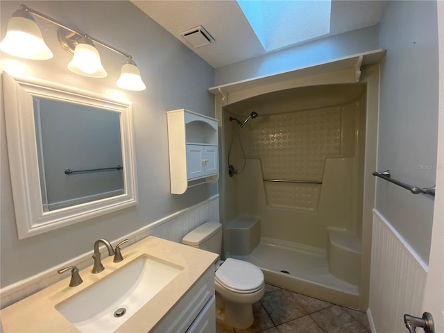 bathroom featuring vanity, walk in shower, a skylight, toilet, and tile patterned floors