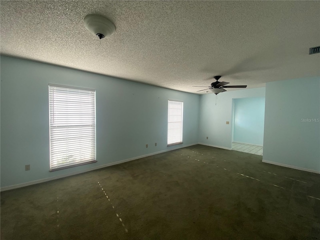 empty room with a textured ceiling, a healthy amount of sunlight, ceiling fan, and dark carpet