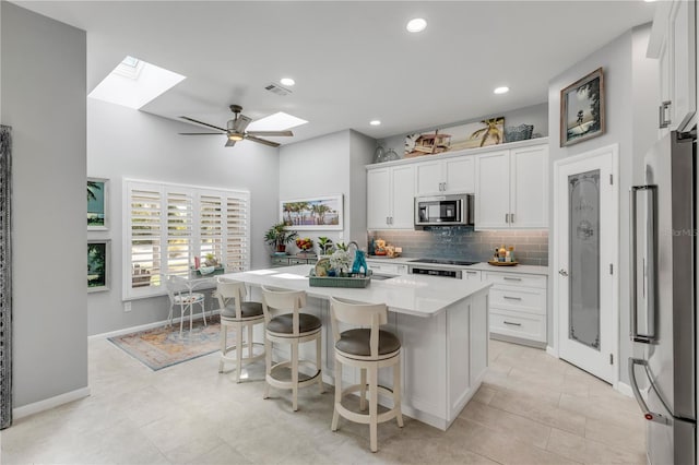 kitchen featuring white cabinets, a center island with sink, appliances with stainless steel finishes, a skylight, and ceiling fan