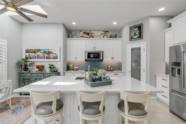 kitchen with an island with sink, white cabinetry, ceiling fan, and appliances with stainless steel finishes