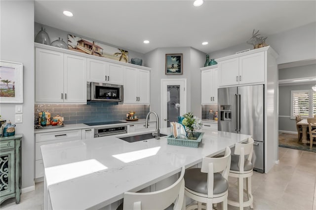 kitchen with light stone counters, white cabinets, sink, a kitchen island with sink, and stainless steel appliances