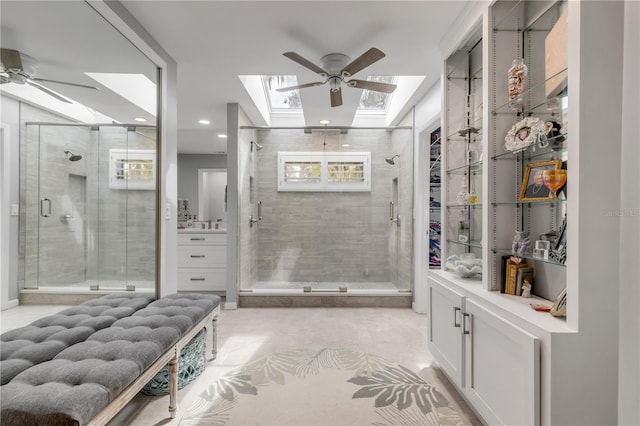 bathroom featuring a skylight, ceiling fan, a shower with door, and vanity