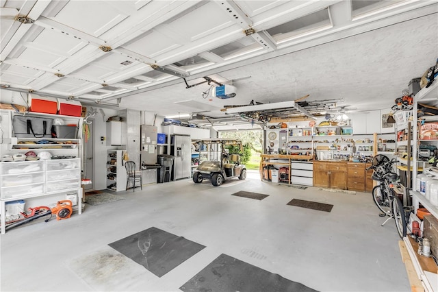 garage with a garage door opener, a workshop area, and stainless steel refrigerator with ice dispenser