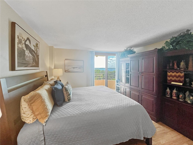 bedroom featuring access to outside, a textured ceiling, and light hardwood / wood-style flooring