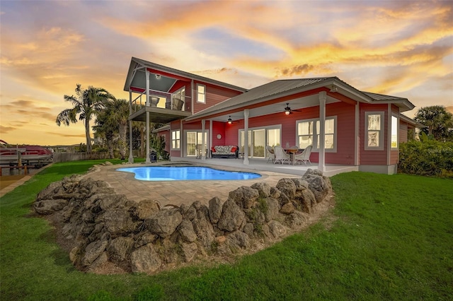 pool at dusk with a lawn, ceiling fan, and a patio area