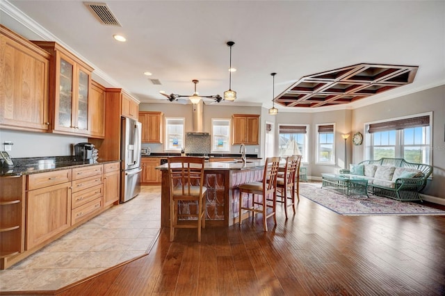 kitchen featuring pendant lighting, light hardwood / wood-style floors, a kitchen island with sink, a breakfast bar area, and stainless steel refrigerator with ice dispenser