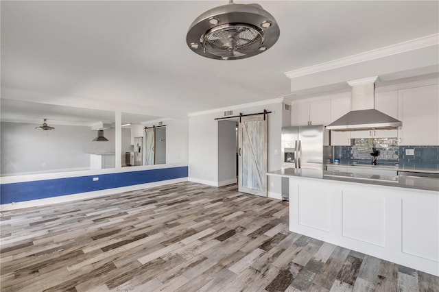 kitchen featuring white cabinets, wall chimney exhaust hood, light hardwood / wood-style flooring, crown molding, and a barn door