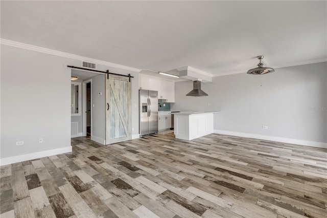 unfurnished living room with a barn door, ornamental molding, and light hardwood / wood-style flooring