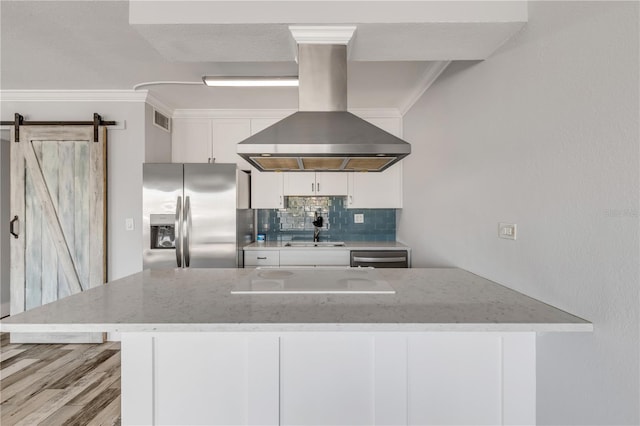 kitchen featuring appliances with stainless steel finishes, white cabinets, a barn door, sink, and wall chimney range hood