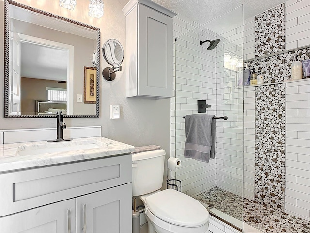 bathroom with a textured ceiling, vanity, toilet, and tiled shower