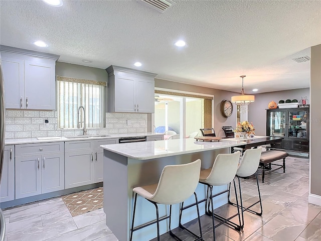 kitchen featuring backsplash, sink, a kitchen island, and hanging light fixtures