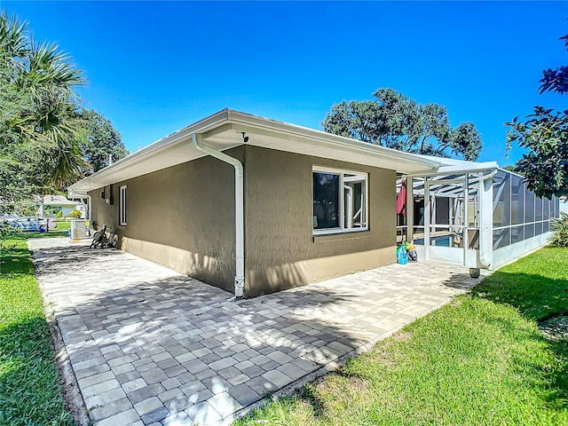 rear view of property featuring a patio, a yard, and glass enclosure